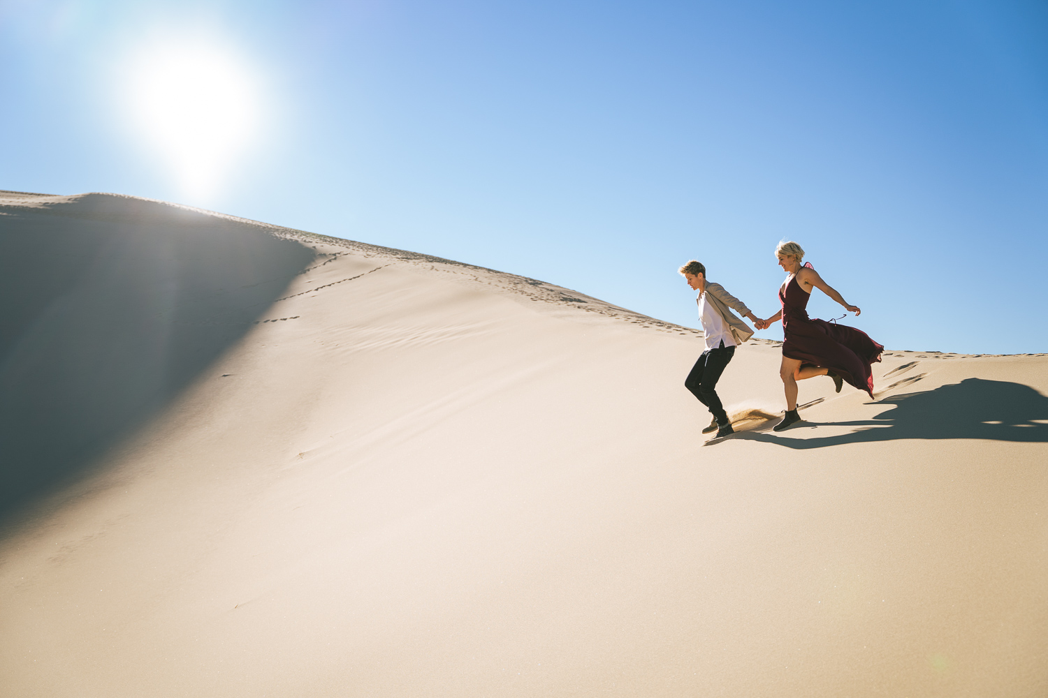 Two brides running through the Death Valley Sand dunes, with a bohemian style flowy red dress