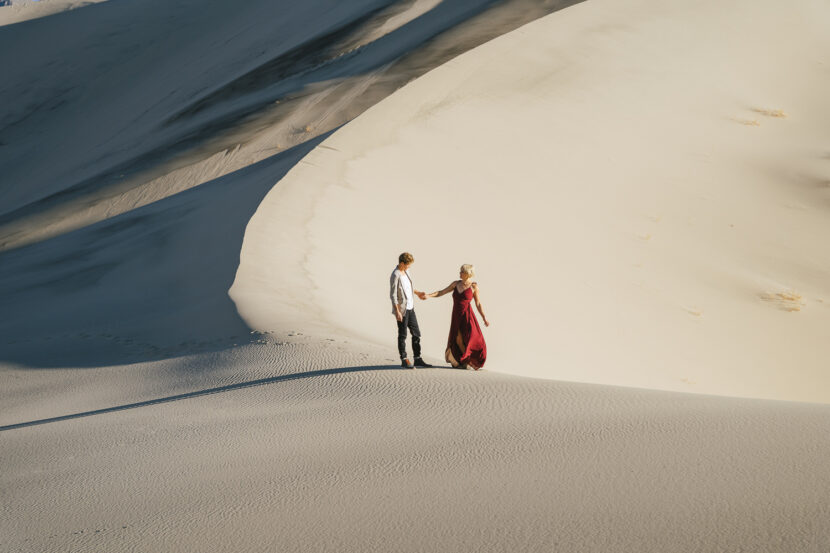 Two brides in the Death Valley Sand dunes, with a bohemian style flowy red dress