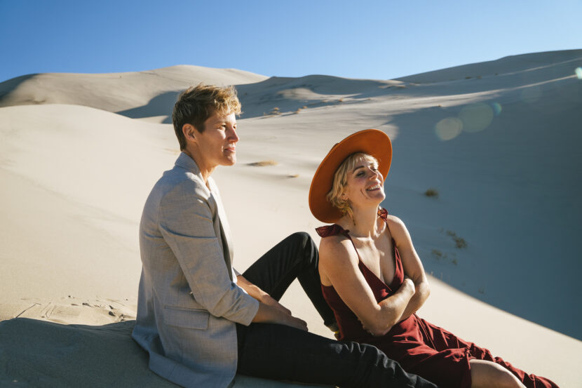 Two brides in the Death Valley Sand dunes, with a bohemian style flowy red dress and hat