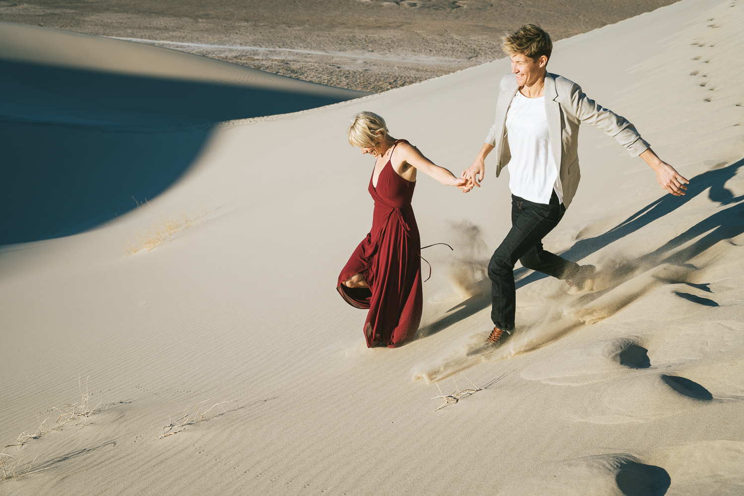 Two brides running through the Death Valley Sand dunes, with a bohemian style flowy red dress